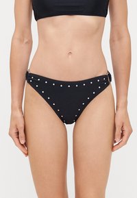 Bas de bikini noir avec des clous en argent, design froncé sur les côtés et texture lisse. Couverture minimale avec une coupe classique.