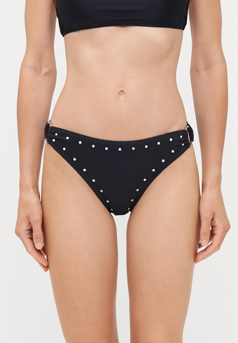 Bas de bikini noir avec des clous en argent, design froncé sur les côtés et texture lisse. Couverture minimale avec une coupe classique.