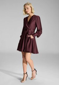Robe portefeuille bordeaux avec de longues manches bouffantes, une taille cintrée et des poches latérales. Tissu lisse avec une jupe évasée et un décolleté en V.