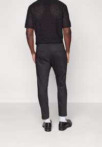 Chemise noire à manches courtes texturée avec des découpes en losange, associée à un pantalon noir tailleur et des chaussures noires. Chaussettes blanches visibles.