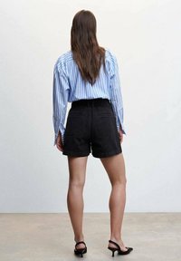 Niebiesko-biała koszula w paski z długim rękawem zestawiona z wysokim stanem czarnych szortów jeansowych. Szorty mają tylne kieszenie i czysty krój.
