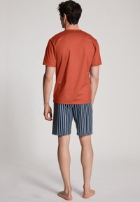 Herenoutfit met een roestkleurig T-shirt en marineblauwe gestreepte shorts. Het T-shirt heeft een ronde hals; de shorts zijn knielang en hebben verticale strepen.