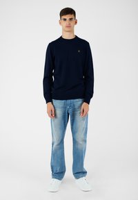 Maglione lavorato a maglia blu navy con scollatura rotonda, abbinato a jeans azzurri chiari e sneakers bianche, offre un look casual e coordinato.