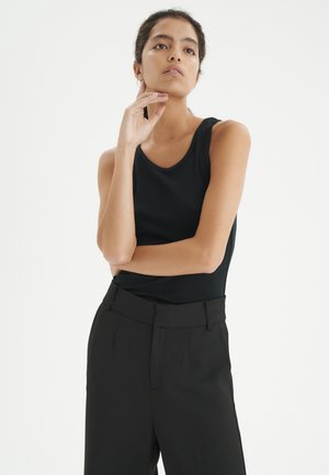 Débardeur noir sans manches en tissu lisse, associé à un pantalon noir taille haute. La tenue présente un design minimaliste et une silhouette ajustée.