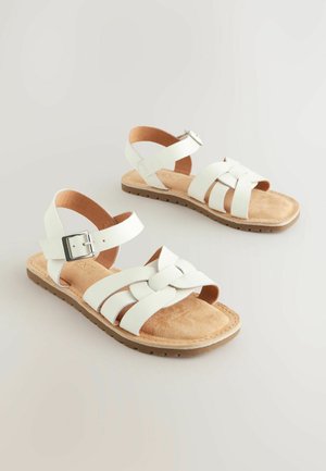 Białe skórzane sandały z plecionym wzorem, regulowanym paskiem na kostce z metalową klamrą oraz brązową teksturowaną podeszwą zapewniającą przyczepność.