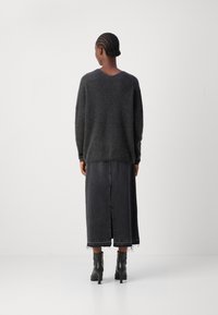 Dunkelgrauer Strickpullover mit V-Ausschnitt, kombiniert mit einem langen schwarzen Jeansrock mit einem Schlitz in der Mitte hinten. Schwarze Stiefeletten mit einem breiten Absatz.