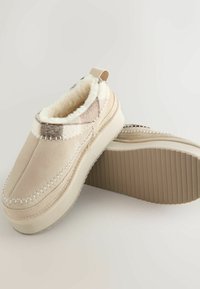 Beige binnenslippers met een zachte, met bont gevoerde binnenkant, met een geruit patroon op de kraag en een geribbelde rubberen zool voor grip.