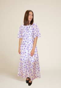 Lilla og gul blomstermønstret maxikjole med korte pufferm og rund hals, laget av lett stoff. Svarte sko.