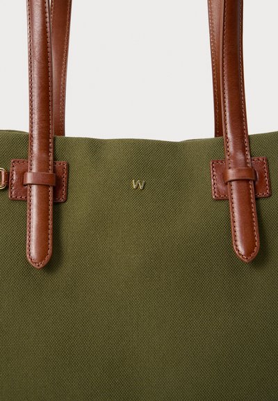 Τσάντα tote σε ελιά πράσινο με υφή, με καφέ δερμάτινες λαβές και μικρό χρυσό έμβλημα "W" τοποθετημένο κοντά στην κορυφή.
