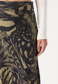 Rakstaina apvalka svārki tumši zaļā un melnā krāsā, ar teksturētu audumu un abstraktiem motīviem. Redzama roka uz jostas vietas.