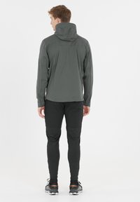 Grijze waterdichte jas met capuchon, nauwsluitende pasvorm en gestructureerde stof, gecombineerd met zwarte taps toelopende pants. Geschikt voor buitenactiviteiten.