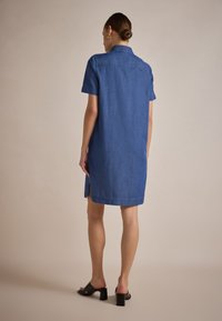 Puvun denim, hihattomat, polvipituinen, vaaleansininen väri, jossa on napituskaulus ja sivuaukot liikkumisen helpottamiseksi.