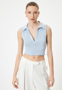 Top corto azul claro hecho de tejido acanalado, con un diseño de cuello en V y cuello. Combinado con pantalones blancos de tiro alto.