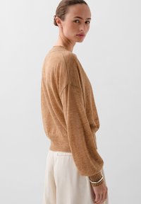 Suéter de punto texturizado en marrón claro, con un corte relajado, puños y dobladillo acanalados. Combinado con pantalones de claro color para un aspecto suave.