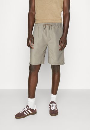 Hellgraue Shorts mit einem elastischen Taillenbund und Kordelzug. Getragen mit braunen Wildledersneakers und weißen Socken. Einfaches, lässiges Design.