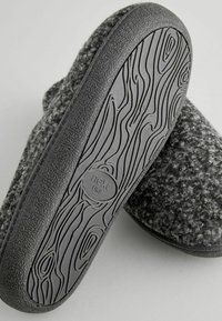 Grau Wollschuh mit strukturierter Oberfläche und grauer Gummisohle mit Holzmaserung. Markenlogo auf der Sohle sichtbar.