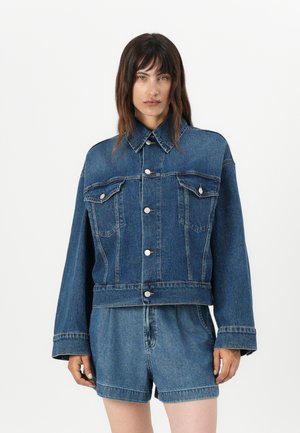 Denimová bunda s límcem, oversized střihem, dvěma náprsními kapsami a předním zapínáním na knoflíky. Modrá látka s klasickou denimovou texturou.