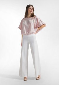 Top rosa extragrande de manga corta con el texto "ATTITUDE", combinado con pantalones blancos de pierna ancha. Tela suave con textura lisa y costuras planas.