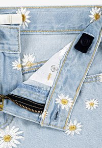 Ανοιχτό μπλε τζιν με λευκές κεντημένες μαργαρίτες και χρυσές λεπτομέρειες. Διαθέτει φερμουάρ, μεταλλικό κουμπί και αντίθετες ραφές.
