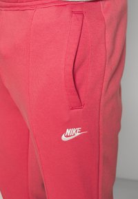 Nike tepláky z jasně růžové bavlny s bočními kapsami a bílým logem na levé noze, s měkkou a hladkou texturou.