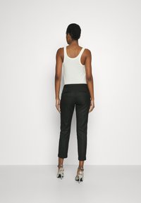 Black tailored pants with a smooth texture and rolled cuffs, paired with a white tank top. The outfit features back pockets and a sleek design.