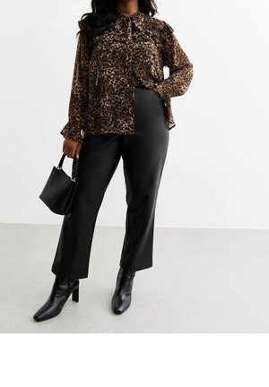 Kvinde iført en brun leopardprint-bluse, sorte korte bukser, sorte ankelstøvler og holder en lille sort håndtaske.