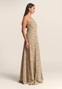 Kaklelis su rišamu kaklu, pagamintas iš smėlio spalvos audinio su juodu gėlių raštu. Plati silueto su ilga suknele, lygia tekstūra ir minimalistiniais akcentais.