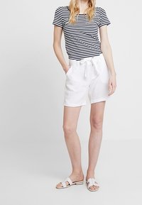 Pantaloni corti bianchi in lino con una vita legata, abbinati a una t-shirt aderente a righe blu e bianche. Indossati con sandali flat bianchi.
