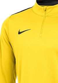 Pullover Nike giallo a maniche lunghe con zip metà, caratterizzato da un accento nero sulla spalla e un logo nero sul petto. Tessuto liscio.
