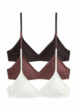 Kobieta w czarnym bikini poprawiająca ręcznik na głowie, stojąc w wodzie po pas przy kamiennym wodospadzie.