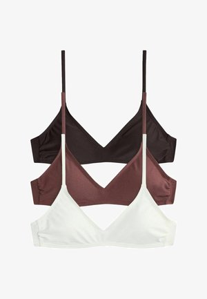 Femeie în costum de baie negru care își ajustează un prosop pe cap, stând până la talie într-o piscină lângă un perete de piatră cu cascadă.