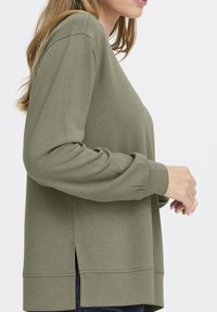 Sudadera verde oliva de manga larga, con un corte holgado, aberturas laterales y puños de punto. Textura suave y diseño sencillo.