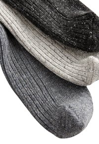 Tre par ribbade strumpor i svart, ljusgrå och mörkgrå med fläckig textur. Varje strumpa har en rundad tå och en mjuk finish.