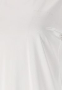 Gros plan sur un tissu blanc uni avec un texte subtilement embossé, montrant une texture lisse et de légers plis.