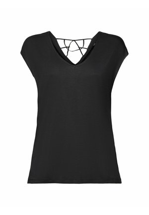 Femme portant un haut noir à manches courtes, un short large couleur moutarde, des baskets blanches, et portant un sac fourre-tout tissé beige.