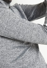 Szara sportowa bluza z teksturowanej tkaniny, z wysokim kołnierzem i dopasowanymi rękawami. Brak widocznych logo lub wzorów.