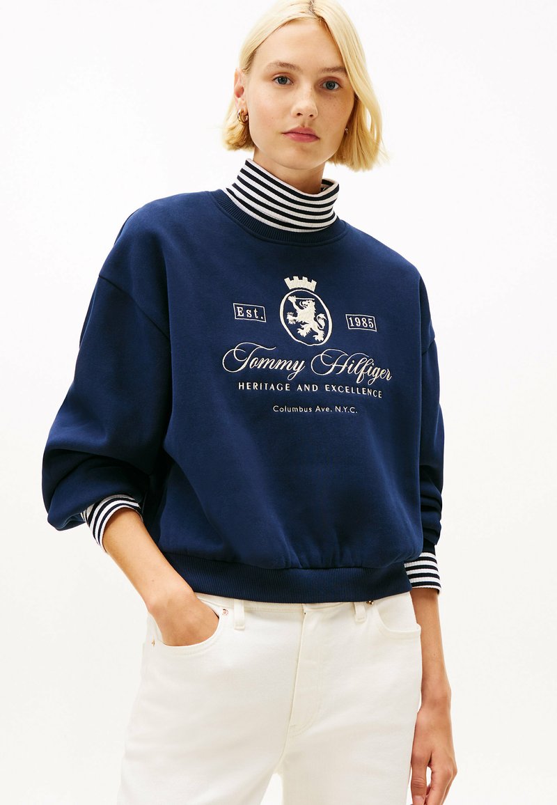 Granatowy sweatshirt z golfem w paski, z białym haftowanym logo i tekstem. Materiał z mieszanki bawełny, luźny krój, ściągacze.