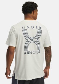 White cotton t-shirt featuring a blue graphic design on the back with the text "UNDER ARMOUR" and a stylized '96' shape.