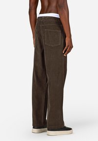 Brūnas krokodila platās kājas bikses ar baltu elastīgu jostu, ar aizmugurējiem kabatām un faktūras auduma dizainu. Stilizētas ar melniem apaviem.