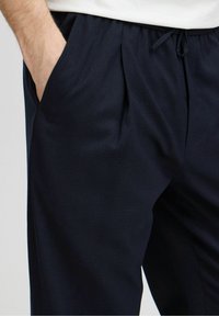 Námořnické kalhoty s texturovanou tkaninou, elastickým pasem, sklady a bočními kapsami. Design je uvolněný pro pohodlí a pohyblivost.