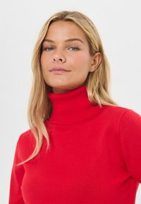 Crvena turtleneck pulover u uskom kroju, s rebrastim detaljima na ovratniku. Glatka tekstura s dugim rukavima.