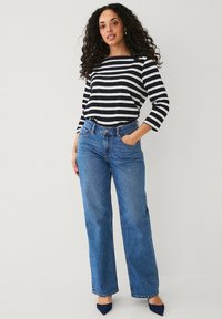 Gestreepte zwart-witte lange mouw top met een bootnek, gecombineerd met hoge taille blauwe wijde broek en blauwe puntige hakken.