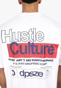 White cotton t-shirt featuring bold red and dark blue text: "Hustle Culture" with additional phrases below. Simple, modern design.