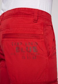 Rode cargoshorts van lichtgewicht stof, met een pocket met een ritssluiting en decoratieve tekst in het grijs, met de tekst "CAMP DAVID BLUE."