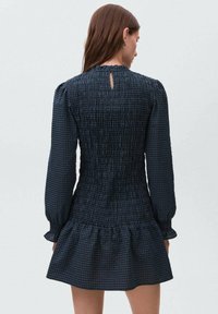 Mornarska karirana obleka z dolgimi napihnjenimi rokavi, smukastim steznikom in razširjenim volanastim robom. Ima odprtino v obliki ključavnice na hrbtu.