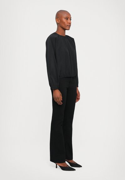 Blusa nera a maniche lunghe con orlo elasticizzato e scollatura rotonda, abbinata a pantaloni neri svasati e eleganti scarpe con tacco alto nere.