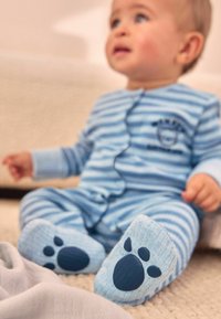 Baby pajamas in light blue with horizontal stripes, featuring a graphic of paw prints on the soles. Soft fabric with a button closure.