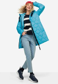 Light blue quilted puffer coat with black zipper, worn over a navy and white striped sweater, paired with light jeans and navy shoes.
