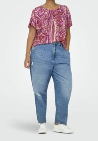Short-sleeve, pink and purple patterned top paired with distressed light blue jeans. Model wears white sneakers; relaxed fit throughout.
