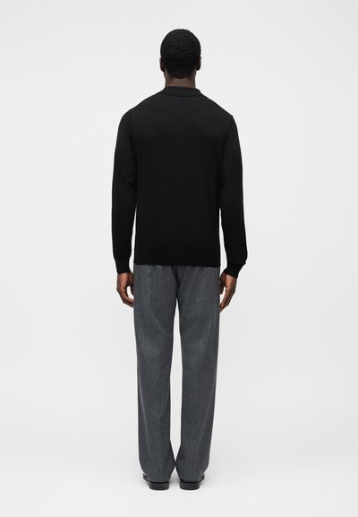 Μαύρο φούτερ με απλό σχέδιο, συνδυασμένο με γκρι παντελόνι με λεπτές ρίγες, από πίσω. Το ύφασμα φαίνεται λείο και casual.